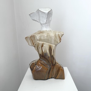 Könnte beinhalten: Keramikskulptur eines Torso mit weißem Kopf und einem Körper, der von Beige zu Braun übergeht. Die Skulptur steht auf einem weißen Sockel. Das Kunstwerk hat ein modernes, abstraktes Design, geeignet für die Inneneinrichtung.