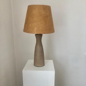 May include: A brown ceramic table lamp with a beige linen lampshade. The lamp has a textured, ribbed design.