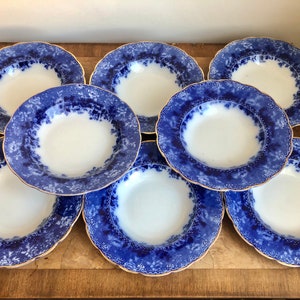 Könnte beinhalten: Ein Satz von acht blauen und weißen Suppenschalen mit goldfarbenem Rand. Die Schalen haben ein Blumenmuster und sind kreisförmig angeordnet.