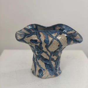 以下が含まれることがあります： 広がった開口部と狭いベースを持つセラミックの花瓶。花瓶は青と白の抽象的なパターンで飾られています。