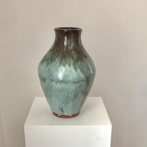 May include: A ceramic vase with a light green and brown glaze. The vase has a rounded body and a narrow neck.