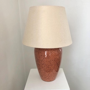 Puede incluir: Una lámpara de mesa de cerámica con una base naranja moteada y una pantalla de tela blanca.