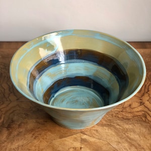 以下が含まれることがあります： 広くて広がった縁と青、茶色、金色のストライプ模様が施された大きな陶器のボウルです。