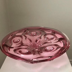 Op de afbeelding: Een roze glazen kom met een draaiend, getextureerd ontwerp. De kom heeft een brede, ondiepe vorm en een licht verhoogd midden.