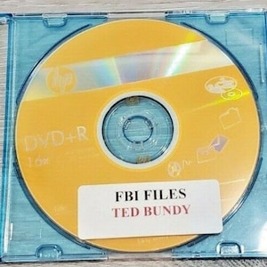 May include: A yellow DVD-R disc in a clear blue jewel case. The disc has a white label with the text "DVD+R 1.6x" and a sticker with the text "FBI FILES TED BUNDY".