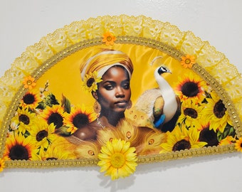 Peut inclure: Un éventail jaune avec une bordure dorée et une bordure en dentelle. L'éventail représente une femme avec un turban jaune et un paon. L'arrière-plan est rempli de tournesols.