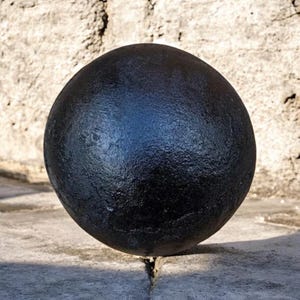 Puede incluir: Una esfera negra sólida con una superficie texturizada. La esfera es redonda y parece estar hecha de metal. El objeto está sobre una superficie de piedra.