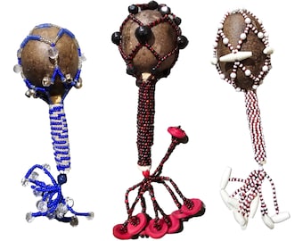 Peut inclure: Trois hochets perlés avec des perles de différentes couleurs. Les hochets sont faits de coques de noix de coco et ont une poignée perlée. Le premier hochet a des perles bleues et blanches, le deuxième a des perles rouges et noires, et le troisième a des perles blanches et rouges.