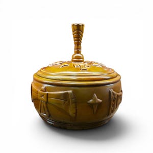 May include: A round, honey-colored wooden lidded container featuring a carved handle on top. The exterior surface is decorated with relief carvings of stylized axes and four-pointed star shapes, showcasing a smooth, polished finish throughout.