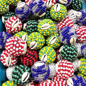 May include: A collection of colorful beaded balls with cowrie shells. The balls are made with various colors of beads, including red, white, blue, green, yellow, and black. The cowrie shells are a natural material and add a unique touch to the balls.