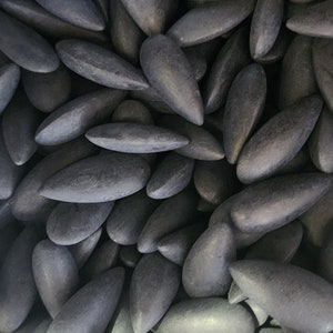 May include: A close-up of a large pile of dark gray, smooth, oval-shaped stones. The stones are arranged in a random pattern, with some overlapping.