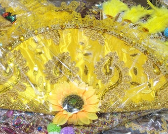 Peut inclure: Un éventail jaune avec des broderies et des paillettes dorées. L'éventail est emballé dans du plastique transparent et a un tournesol sur le dessus.