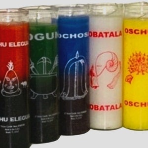 May include: Six glass candle jars with different colored wax and labels. The labels have the names "Eshu Eleggua", "Og&uacute;n", "Ochos&iacute;", "Obatala", "Osch&uacute;n" written on them.