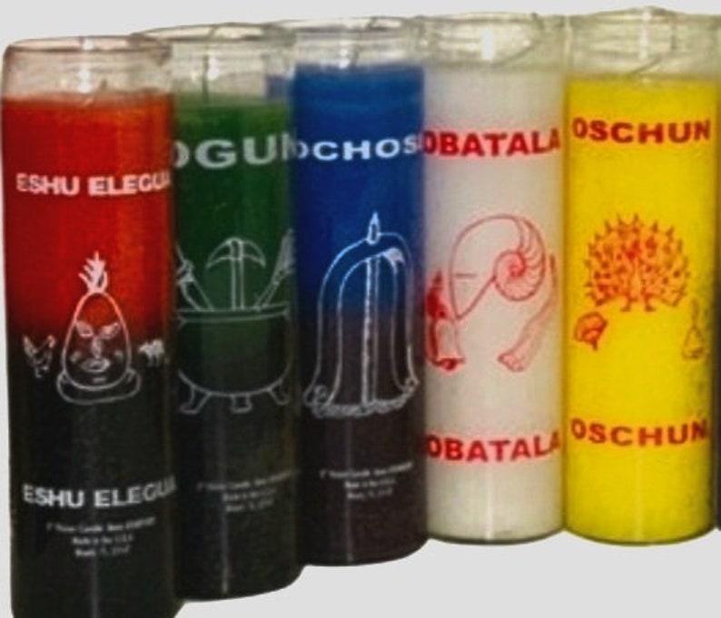 May include: Six glass candle jars with different colored wax and labels. The labels have the names "Eshu Eleggua", "Og&uacute;n", "Ochos&iacute;", "Obatala", "Osch&uacute;n" written on them.