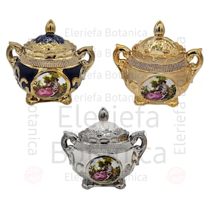 Op de afbeelding: Drie keramische serveerschalen met deksels. De schalen zijn versierd met gouden, zilveren en blauwe verf. Elke schaal heeft een bloemmotief met een stel in het midden. De schalen zijn allemaal even groot en even gevormd.