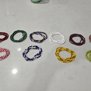Peut inclure: Une collection de 10 perles de taille pour la taille, chacune avec une combinaison de couleurs différente. Les perles sont disposées en rangée sur une surface blanche.