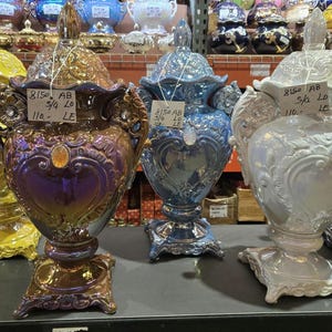 May include: Four decorative ceramic vases with ornate designs. The vases are in shades of yellow, purple, blue, and white. The vases are all approximately 28 cm tall and have a price tag of 110 LE.