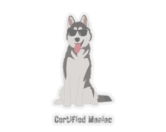 May include: A sticker featuring a grey and white husky dog wearing black sunglasses with its tongue hanging out. Below the dog, the text Certified Maniac is printed in a dark grey, distressed font. The design has a white border outline.