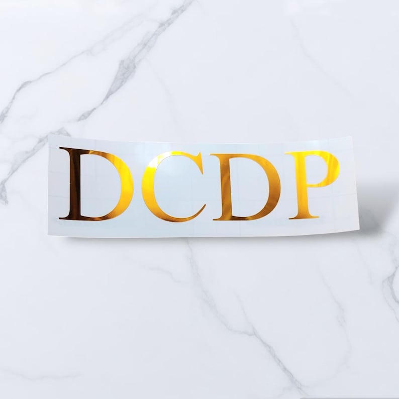 May include: Gold vinyl decal with the letters "DCDP" in a serif font.