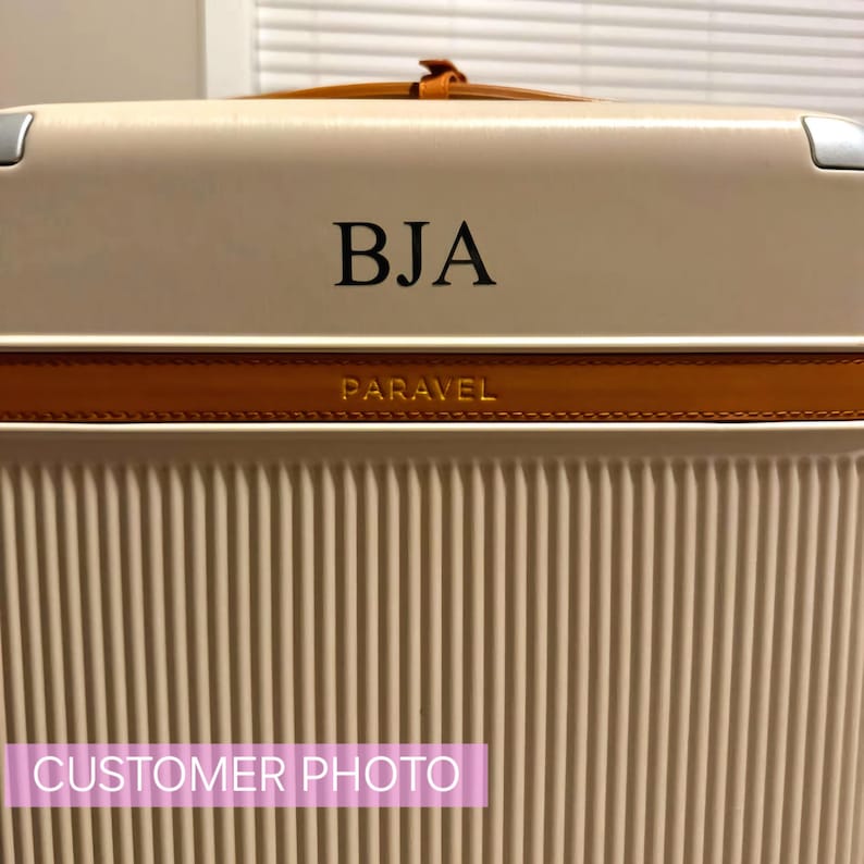 May include: A beige suitcase with a brown leather trim and the word "PARAVEL" embossed on the trim. The suitcase has a personalised monogram "BJA" on the front.