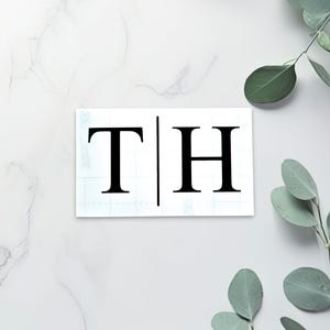Könnte beinhalten: Ein weißer Hintergrund mit einem schwarz-weißen Monogramm der Buchstaben "T" und "H", die durch eine vertikale Linie getrennt sind.
