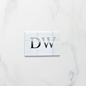 May include: A white sticker with the letters "DW" in silver foil.