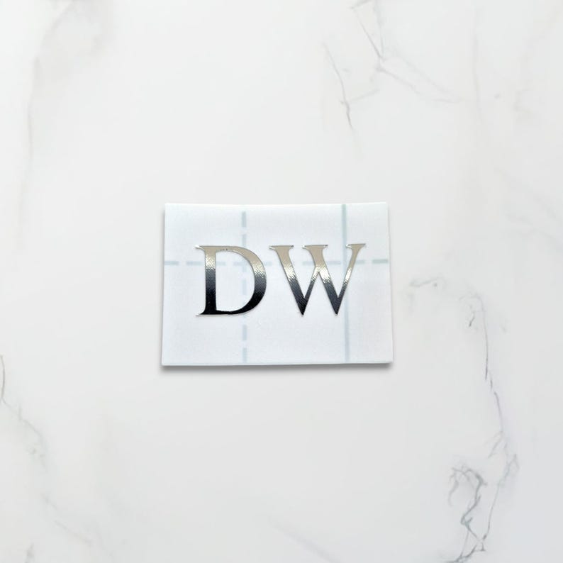 May include: A white sticker with the letters "DW" in silver foil.