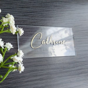 Puede incluir: Tarjeta de lugar de acrílico transparente con el nombre "Catherine" escrito en letras doradas.