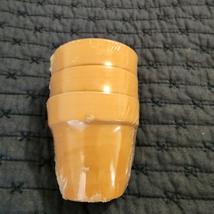 May include: A stack of four terracotta plant pots wrapped in plastic. The pots are a light brown color and are all the same size.