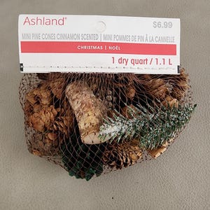 May include: A bag of cinnamon scented mini pine cones and pine branches for Christmas decor. The bag is labeled "Ashland" and contains 1 dry quart or 1.1 liters of pine cones and branches. The price is $6.99.