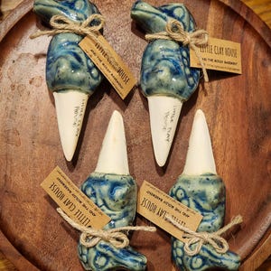May include: Four ceramic plant waterers with a blue and white swirl design, tied with twine and labeled "Little Clay House". The waterers have a cone-shaped base and are displayed on a wooden tray.