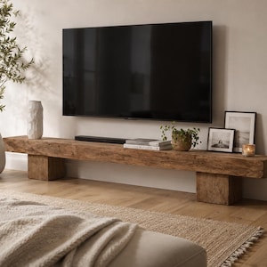 May include: A long, low-profile television console crafted from reclaimed wood with a rough, textured surface. The rectangular beam rests on two thick, block-style wooden legs, providing a sturdy base for a flat-screen television mounted above.