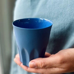 Könnte beinhalten: Eine blaue Keramiktasse mit strukturierter Außenseite. Die Tasse wird in einer Hand gehalten.