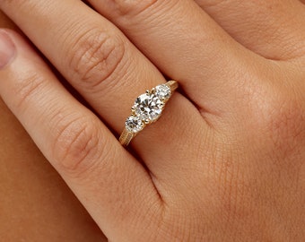 May include: A gold three-stone engagement ring with a large round center stone and two smaller round accent stones.