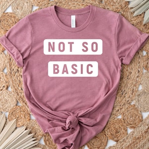 May include: A mauve colored t-shirt with the text "NOT SO BASIC" printed in white.