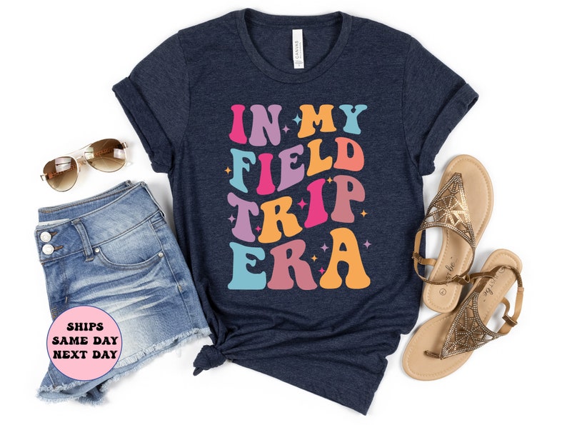 K&ouml;nnte beinhalten: Ein marineblaues T-Shirt mit dem Text "IN MY FIELD TRIP ERA" in bunter Retro-Schrift.