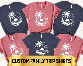 May include: A collection of short-sleeved t-shirts in dark blue and dusty rose colors. Each shirt features a white circular graphic of a palm tree, a sun, and the text "CANCUN 2026" and "WILSON FAMILY TRIP". A gold banner displays "CUSTOM FAMILY TRIP SHIRTS".