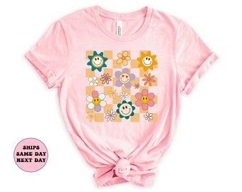 May include: Pink t-shirt with a checkered pattern featuring colorful flowers and smiley faces.