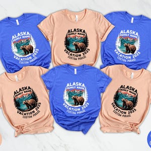 Peut inclure: Plusieurs t-shirts de couleurs vari&eacute;es, notamment bleu et p&ecirc;che. Chaque t-shirt arbore un motif circulaire avec l'inscription "Alaska Vacation 2025" et une illustration d'ours. Id&eacute;al pour les vacances en famille.