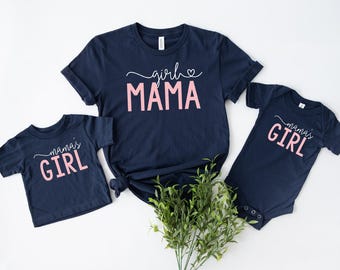 May include: Two navy blue t-shirts with pink text. The larger shirt says "girl mama" with a heart. The smaller shirt says "mama's girl".