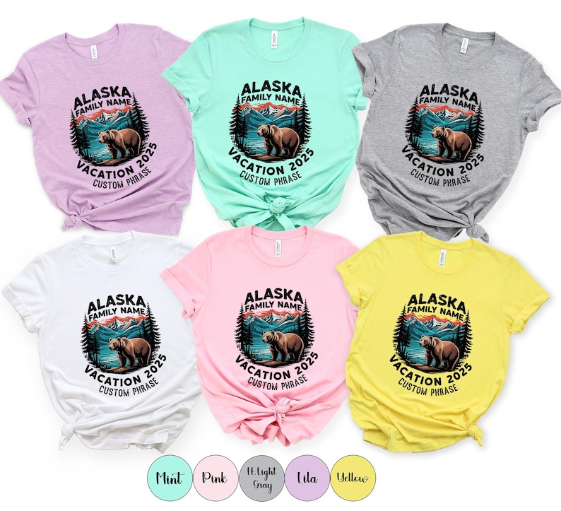 Peut inclure: Plusieurs t-shirts de couleurs vari&eacute;es avec un motif circulaire repr&eacute;sentant un ours, des montagnes et des arbres. Le texte indique "Alaska Family Name Vacation 2025 Custom Phrase". Les t-shirts sont en menthe, rose, gris clair, lilas, jaune et blanc.