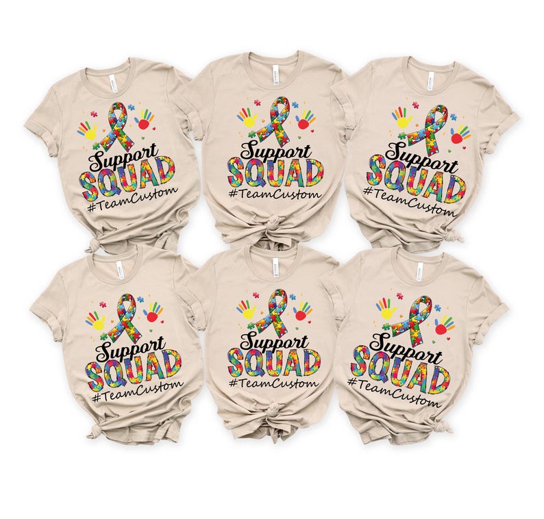 May include: Six beige t-shirts with a colorful puzzle piece ribbon, handprints, and the text "Support Squad #TeamCustom" printed on the front.