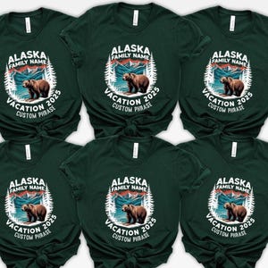 Peut inclure: T-shirts vert fonc&eacute; avec un motif circulaire repr&eacute;sentant un ours brun, des montagnes et le texte "ALASKA FAMILY NAME VACATION 2025 CUSTOM PHRASE". Le motif est en blanc et dans les tons de marron et de bleu.