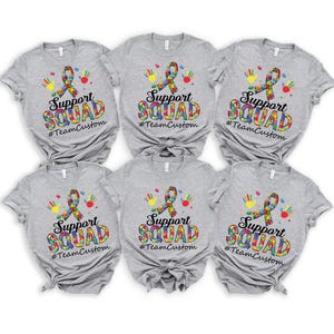 May include: Six gray t-shirts with a colorful puzzle piece ribbon and the text "Support Squad #TeamCustom" printed on the front.