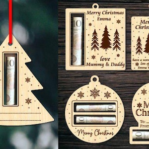 Puede incluir: Cuatro adornos navideños de madera con ranuras para dinero en efectivo. Los adornos tienen forma de árbol, bola y dos rectángulos. Los adornos están decorados con copos de nieve y el texto "Feliz Navidad".