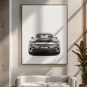 May include: A black and white photograph of a silver Porsche 911 Turbo S, viewed from the rear, parked in front of a white wall.
