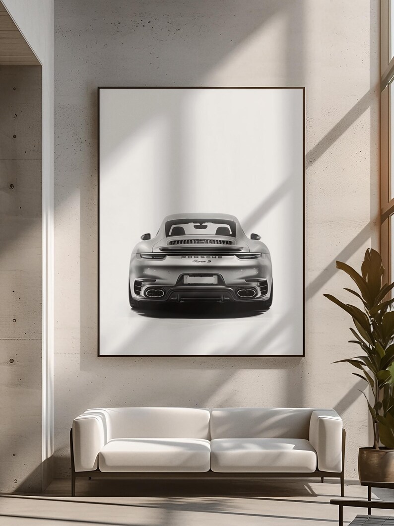 May include: A black and white photograph of a silver Porsche 911 Turbo S, viewed from the rear, parked in front of a white wall.