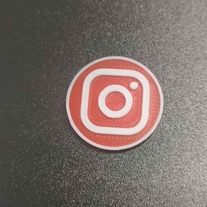 Pu&ograve; includere: Logo Instagram rotondo, rosso e bianco. Il logo presenta un contorno bianco e un'icona della fotocamera bianca al centro. Lo sfondo &egrave; di colore grigio scuro.
