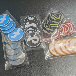 Pu&ograve; includere: Vari adesivi rotondi in sacchetti di plastica trasparente. I disegni includono un logo 'f' blu e bianco, un logo 'S' in bianco e nero, un design geometrico multicolore, cerchi rossi e cerchi arancioni con testo.