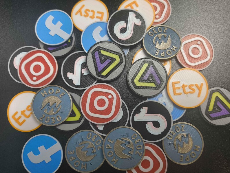 Pu&ograve; includere: Una collezione di gettoni circolari colorati con loghi di social media e piattaforme di e-commerce. I loghi includono Etsy, Instagram, Facebook e TikTok. Alcuni gettoni presentano la scritta "HOPE 2030" e un disegno del globo. I gettoni sono in vari colori, tra cui blu, rosso e arancione.